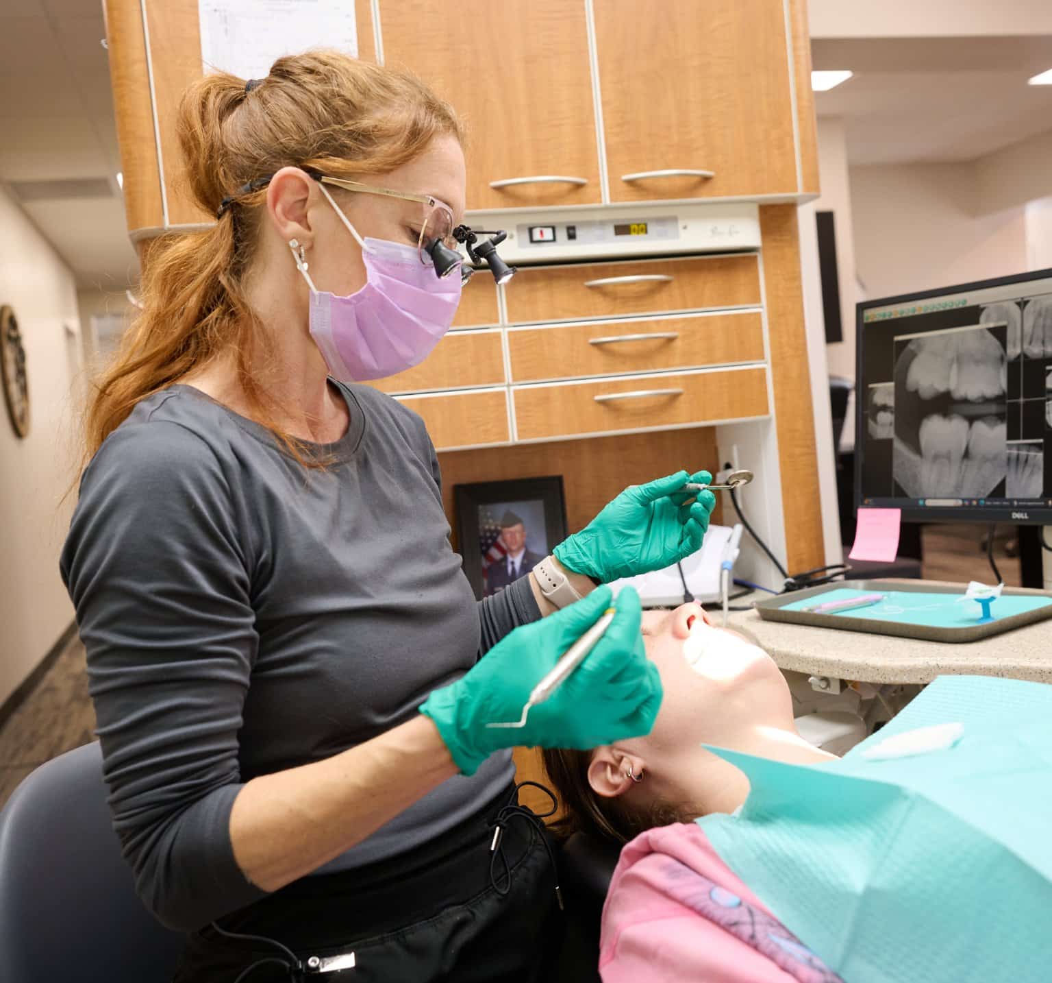 Harrison Family Dental team member wearing loupes treating a patient, with digital X-ray images on the monitor behind her